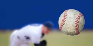 A baseball in mid-air with a pitcher in the background preparing to throw