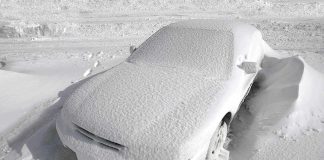 A car completely covered in snow, surrounded by a winter landscape