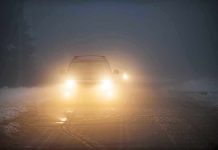 Two cars with headlights on driving in foggy conditions on a snowy road