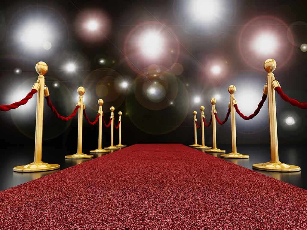 A red carpet lined with gold stanchions and ropes under bright spotlights
