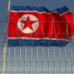 North Korea’s NEXT Dictator Drives Tank Barbed wire fence with North Korean flag behind.