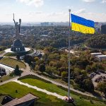 Large Ukraine flag with cityscape in background.