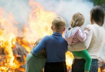 Three children and adult watching large fire outdoors