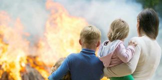 Three children and adult watching large fire outdoors