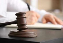 Judges gavel on desk with person writing.