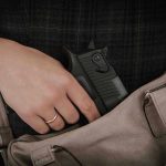 Hand placing handgun into beige handbag.