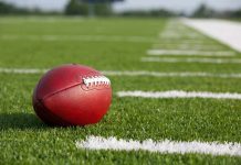 Football Star BITES Woman A red American football resting on a green artificial turf field