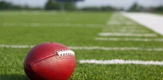 A red American football resting on a green artificial turf field
