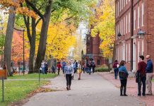 Students walking on a campus path surrounded by autumn trees and brick buildings