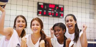 Four female volleyball players celebrating in a gymnasium