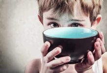 A child with a serious expression holding a bowl close to their face