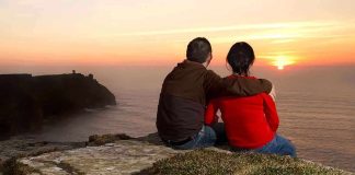 A couple sitting on a cliff watching the sunset over the ocean