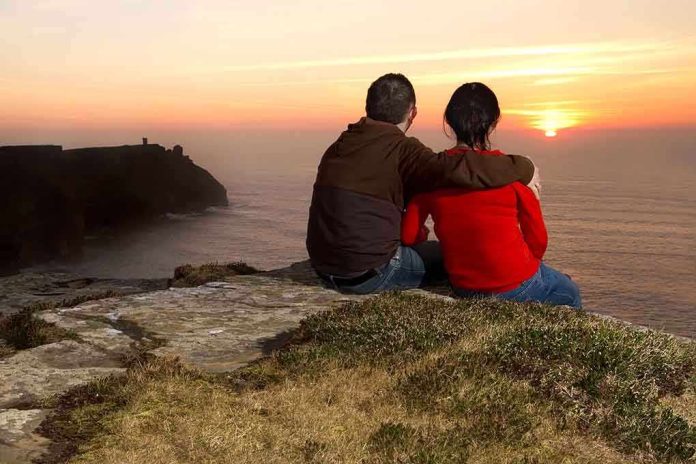 A couple sitting on a cliff watching the sunset over the ocean