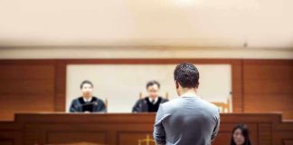 Man stands in courtroom before judges and stenographer.