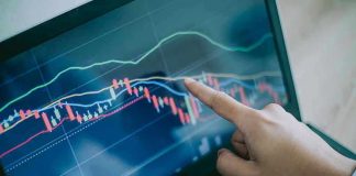 Finnish Data RATTLES Gender Medicine Hand pointing at stock market graph on laptop screen.