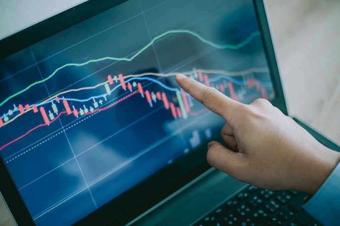 Hand pointing at stock market graph on laptop screen.