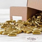 Box of brass bullets spilled on wooden surface.