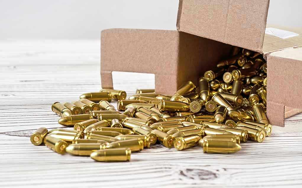 Box of brass bullets spilled on wooden surface.