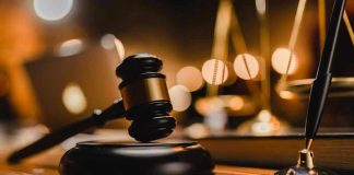 Gavel on wooden table with scales in background.