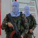 Masked soldiers holding rifles in front of a monument.
