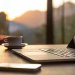 Laptop, coffee cup, and phone on wooden table.