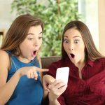 Two women look surprised at a phone.