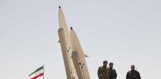 Military personnel beside missiles and Iranian flag.