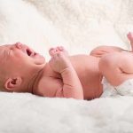A newborn baby lying on a soft blanket, crying with a distressed expression