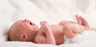 A newborn baby lying on a soft blanket, crying with a distressed expression