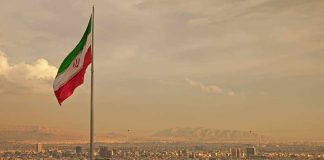 Iranian flag waving over a city skyline with mountains in the background