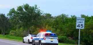 Police car with flashing lights pulling over a white vehicle beside a speed limit sign