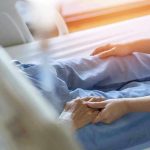 Hospital patient holding visitors hand reassuringly.