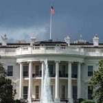 White House with American flag and fountain, stormy sky.