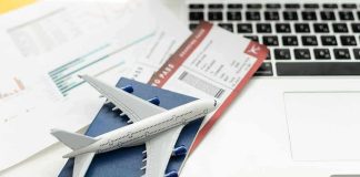 A model airplane on a blue passport next to a laptop and boarding pass