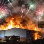A large building engulfed in flames with fireworks in the sky