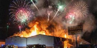 A large building engulfed in flames with fireworks in the sky