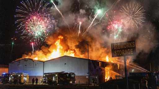 A large building engulfed in flames with fireworks in the sky