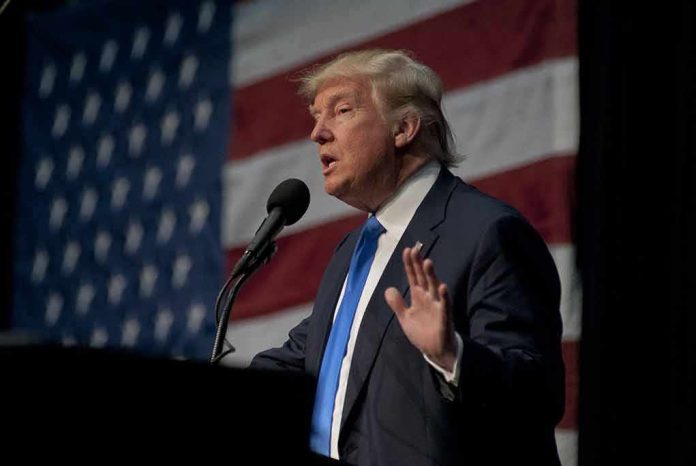 man in suit speaking at a podium with a US flag backdrop