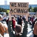 Person holding protest sign above head at a crowded rally
