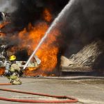 Gas Truck EXPLODES on Freeway into Fireball Firefighter spraying water on a vehicle engulfed in flames