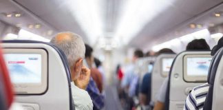 Airplane cabin aisle with passengers seated and seatback screens