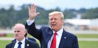Donald Trump waves while walking outdoors with security nearby