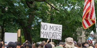 Crowd holds No More Mandates sign at protest.
