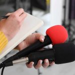 Deadly Trump Pills FLOOD The Streets Journalist holding two microphones while writing in a notebook