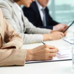 Close-up of hands in business attire during a meeting, writing notes and reviewing documents