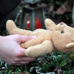 Hands holding a teddy bear near a grave