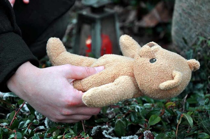 shutterstock_1064488499 Hands holding a teddy bear near a grave
