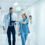 Doctor and nurse walking in a hospital corridor reviewing a tablet