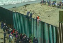 People climbing a tall beachside border fence
