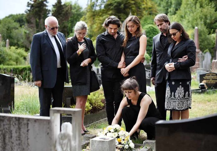 shutterstock_1230694315 Mourners gathered at a graveside placing flowers